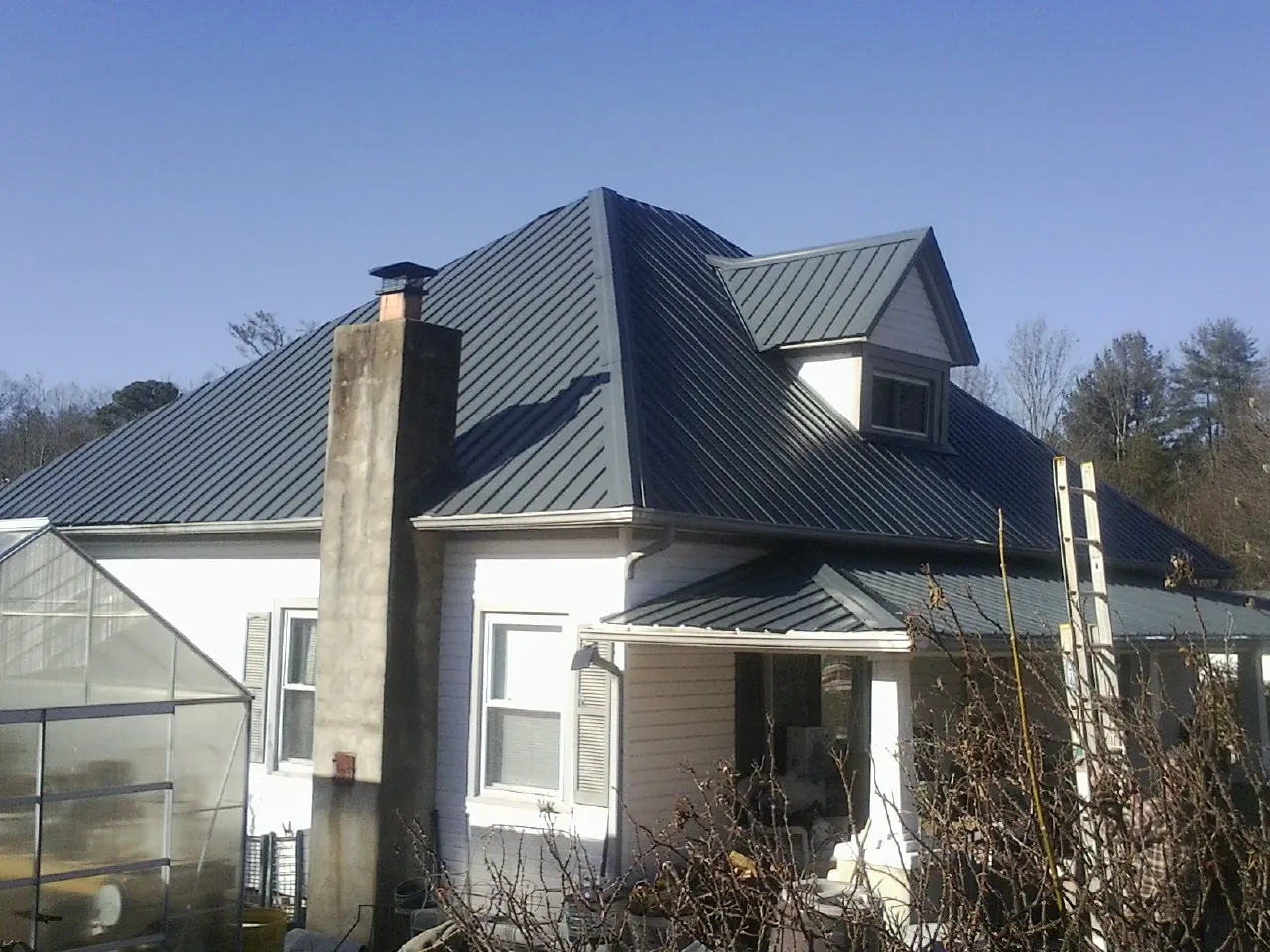 Dark blue standing seam metal roof on a white farmhouse with dormer — Slate & Tile Roof Repair by Roofing Brothers in Malin