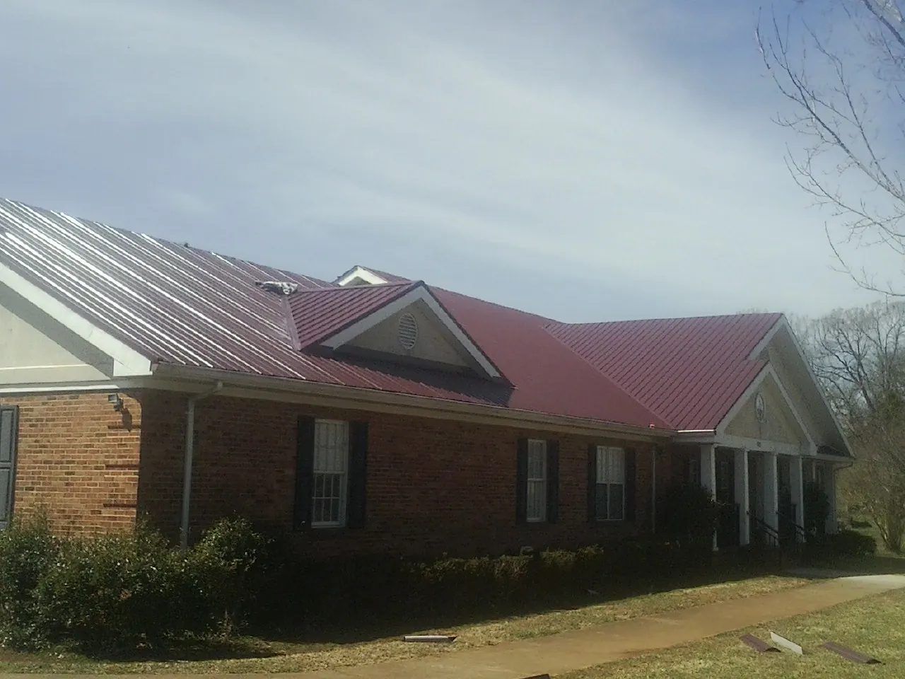 Red metal roof with gabled entries on a long brick building, from a Hail Damage Roof Repair job in Malin