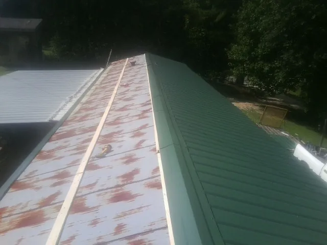 Old rusted panels beside newly installed green metal roofing — Wind Damage Roof Repair by Roofing Brothers in Malin
