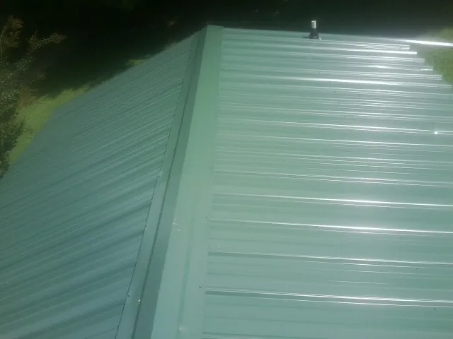 New green metal panels meeting at the ridge of a roof — Flat Roof Repair work by our crew in Malin