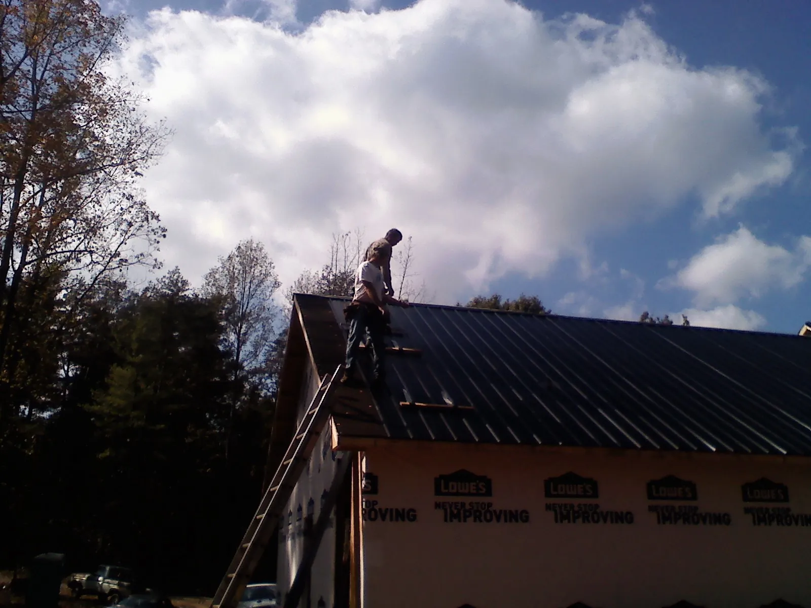 Roofer fastening dark metal panels high against a cloudy sky, from a Roof Inspection job in Malin