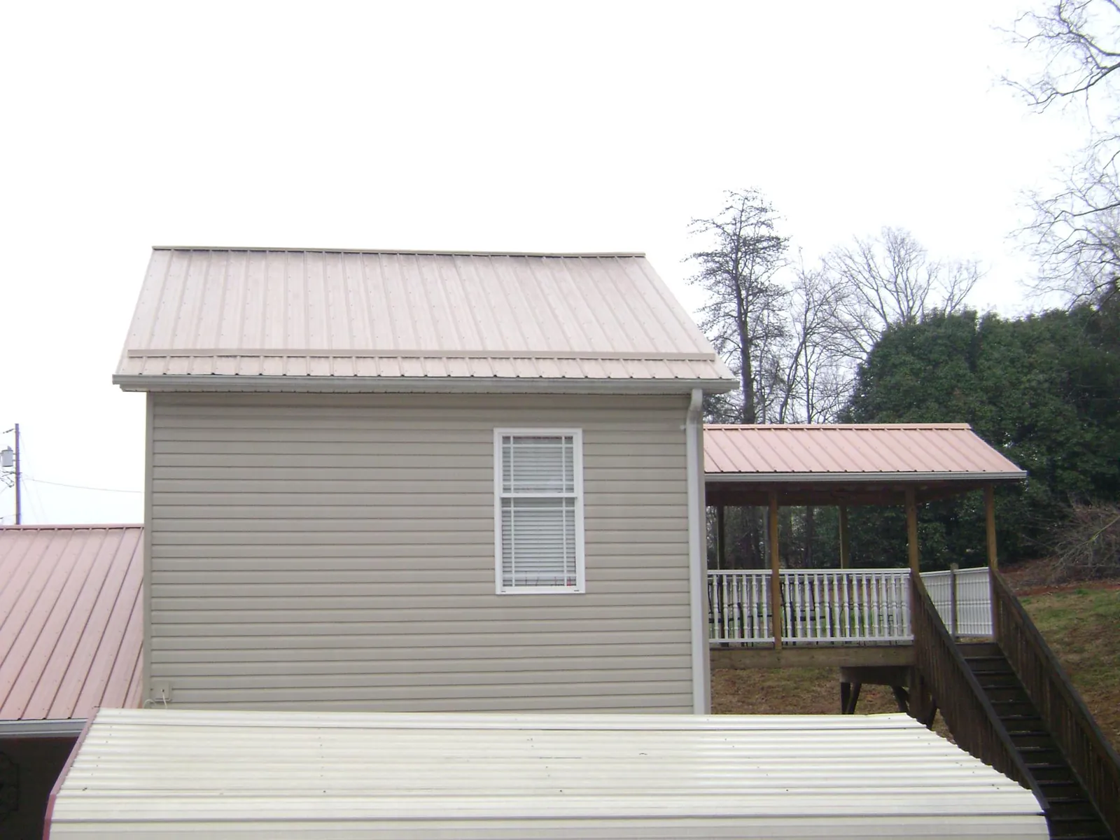 Tan metal roofs on a two story addition and attached porch, from a Roof Replacement job in Malin